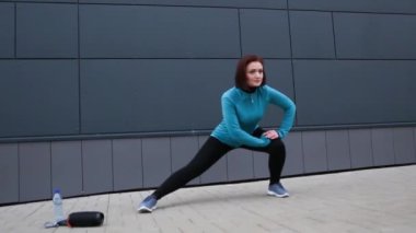 Bir kadın dışarıda spor egzersizleri yapıyor, genişleticiyle çömeliyor. Evde antrenman, spor salonu dışında, yeni bir gerçeklik.