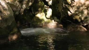 Dağ nehrindeki berrak su gurulduyor ve dalgalanmalar gösteriyor, sarı kumlu tabanı görebilirsiniz. Kayaların arasında su kaynıyor..