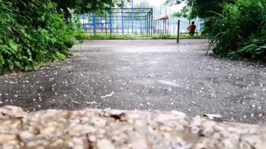 Büyük dolu asfalta ve evin eşiğine düşüyor ve yüzeyden sekiyor. Doğal olaylar, ilkbahar ve yaz öğeleri, avlu manzarası.