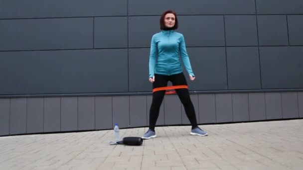 女性は外でスポーツの練習をし 拡大器でスクワットします 自宅でトレーニング ジムの外 新しい現実 — ストック動画