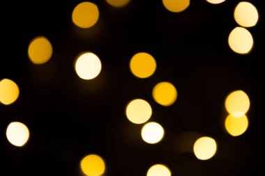 Sarı ve altın renkli çelenkler siyah arka planda bulanık. Bokeh of fly circle in the defocus. Noel ve yeni yılın şenlikli atmosferi. Arkaplanı kutla