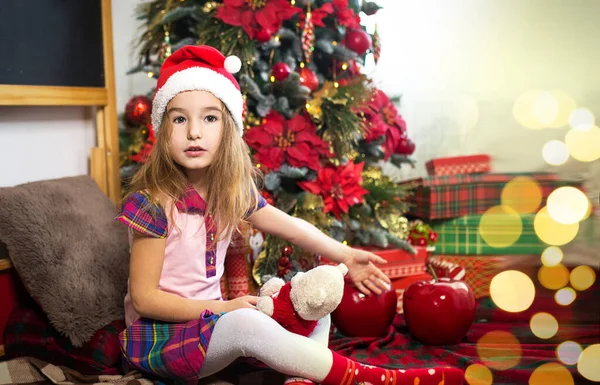 Een Klein Meisje Met Een Kerstmuts Bij Een Kerstboom Wijst — Stockfoto