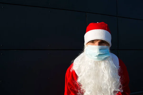 Santa Claus with white beard in red coat in a medical mask. Christmas in the coronavirus pandemic, seasonal diseases, SARS and pneumonia in the holidays. Protection from viruses in the new year.