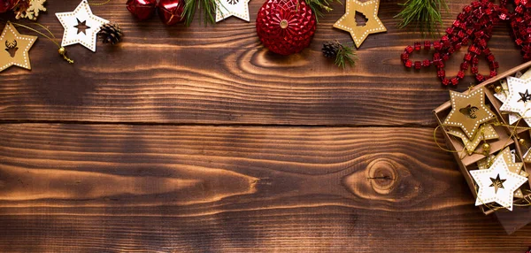 Ahşap bir arka planda Noel dekoru olan çerçeve. Yeni yıl, tatil atmosferi, yeşil ladin dalları, süslemeler: yıldızlar, hediye kutusu, boncuklar, top, çanlar, koniler. Metin için boşluk, düz uzanma