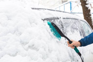 Bir adam kar yağdıktan sonra arabadan kar temizler. Mavi ceketli bir el ve beyaz vücutlu bir araba süpürgesi. Kış havası koşulları