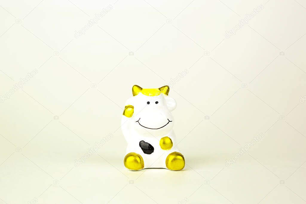 Ceramic toy white cow with gold spots-a symbol of the new year 2021. Piggy Bank for money. White background, copy space