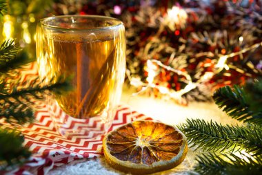 Masada sıcak çay ve tarçın çubukları ve Noel süsüyle şeffaf çift duvarlı cam bardak bardak. Yeni yıl atmosferi, kurutulmuş portakal, çelenk ve süs, ladin dalı, sıcacık