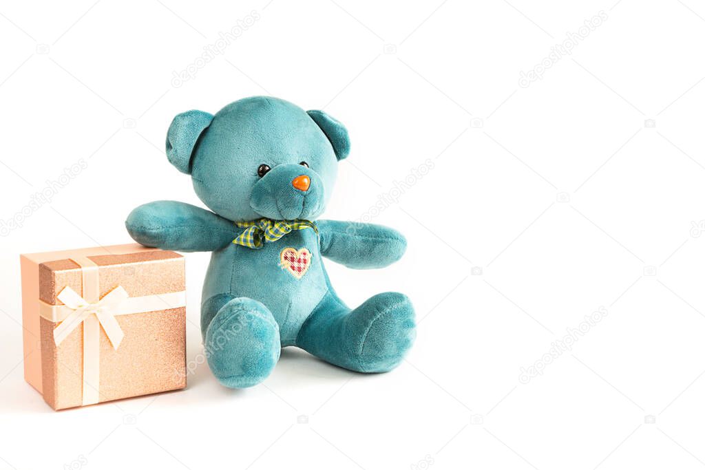 Turquoise soft teddy bear with an embroidered heart holds a gift box and a bow on a white background. Children's toy. Love, a gift to holiday, a declaration of love, Valentine's day. Copy space