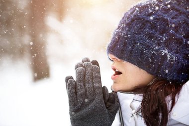 Örgü şapkalı kadın gözlerini soğuk soğuk kapadı ve nefesiyle ellerini ısıttı. Açık hava aktiviteleri, ilkbahar, kış, kar erir, kar, buz. Havadan saklanmak, rahatlık. Yakın plan.