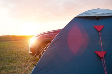 Arabanın yanına turist çadırı kurduk. Ev turizmi, aktif yaz gezisi, aile maceraları, otomobil kampı. Eko-turizm. Arabayla seyahat et. Gün batımı, gün doğumu, gece yolda. Boşluğu kopyala