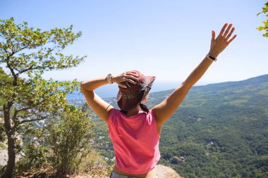 Şapkalı kadın dağdan denize ve ormana kadar panoramik manzaraya bakıyor. Turist, yürüyüş, seyahat. Aktif eko-turizm, sağlıklı yaşam tarzı, macera
