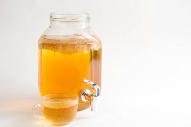 Kombucha-a drink made from tea mushroom in a glass jar with a tap. Transparent mug with a yeast drink made from a Japanese mushroom-jellyfish. White background, healthy food. Copy space