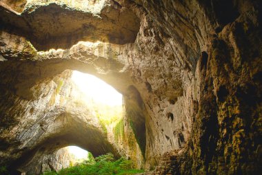 Bulgaristan 'daki Devetashka mağarası - doğal eğlence. Tepesinde yuvarlak delikler olan büyük taş bir mağaranın yüksek kemerleri, mağaranın içinde çitleri olan turistik bir yol.. 