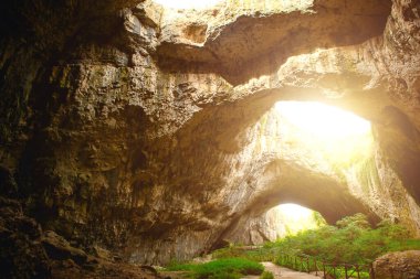 Bulgaristan 'daki Devetashka mağarası - doğal eğlence. Tepesinde yuvarlak delikler olan büyük taş bir mağaranın yüksek kemerleri, mağaranın içinde çitleri olan turistik bir yol.. 