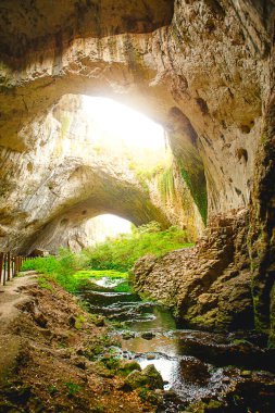 Bulgaristan 'daki Devetashka mağarası - doğal eğlence. Tepesinde yuvarlak delikler olan büyük taş bir mağaranın yüksek kemerleri, mağaranın içinde çitleri olan turistik bir yol.. 