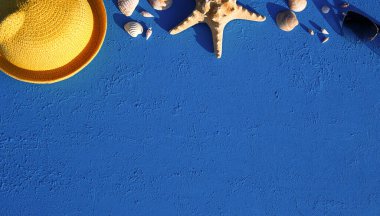 Deniz temalı plaj aksesuarları olan çerçeve: sarı hasır şapka, güneş gözlüğü, deniz yıldızı ve mavi arka planda deniz kabuğu. Tatil konsepti, deniz yolculuğu, ultraviyole koruma, yüzme. Uzayı kopyala Düz Yatay