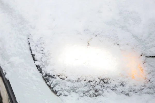 The glowing car headlights in the snow. Cleaning the car after a snowfall. Danger on the road in bad weather conditions in winter.