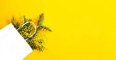 Beyaz bir hediye paketinde bir buket mimoza. Bahar alışverişi, Uluslararası Kadınlar Günü için hediyeler ve promosyonlar. Sarı arkaplan, kopyalama alanı.