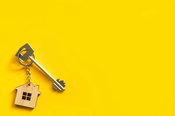 Key chain in the shape of wooden house with key on a yellow background. Building, design, project, moving to new home, mortgage, rent and purchase real estate. Copy space