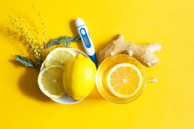 Bir fincanda tıbbi çay, zencefil, limon, soğuk mevsimde bağışıklık sistemini güçlendiren akasya, termometre, düz bir şekilde. Sarı arka planda sağlık ve malzemeler için vitamin içeceği. 