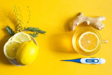 Bir fincanda tıbbi çay, zencefil, limon, soğuk mevsimde bağışıklık sistemini güçlendirir, termometre ve fotokopi alanı, notlar için çarşaf. Sarı arka planda sağlık ve malzemeler için vitamin içeceği. 