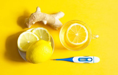 Fincanda tıbbi çay, zencefil, soğuk mevsimde limon güçlendirme bağışıklık sistemi. Sağlık ve malzemeler için vitamin içeceği, sarı arka planda termometre. Grip, soğuk algınlığı, bağışıklık, ateş, ateş düşürücü.