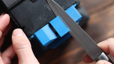 Evdeki elektrikli bileyiciye bıçak keskinleştirmek. Adamın eli bıçağı mavi bileyicilerin arasından geçirir, makinede toz uçar..