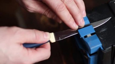 Evdeki elektrikli bileyiciye bıçak keskinleştirmek. Adamın eli bıçağı mavi bileyicilerin arasından geçirir, makinede toz uçar..