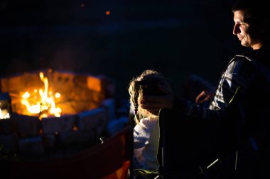 Baba ve kızı, yazın açık havada, ateşin yanında otururlar. Aile kamp gezisi