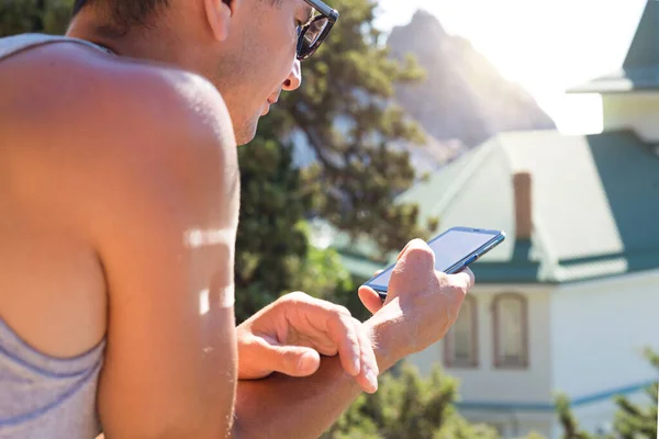 A male tourist uses a smartphone while traveling. Navigation, sightseeing search, mobile roaming, online travel guide. Beautiful view of the hotel and the mountains.