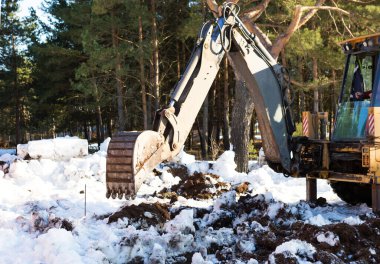 Buldozer kovası inşaat için bir çukur kazıyor. Evin temeli, toprak işleri. Kazıcı bir kova ile toprağı kazar. Tarım, tarım.
