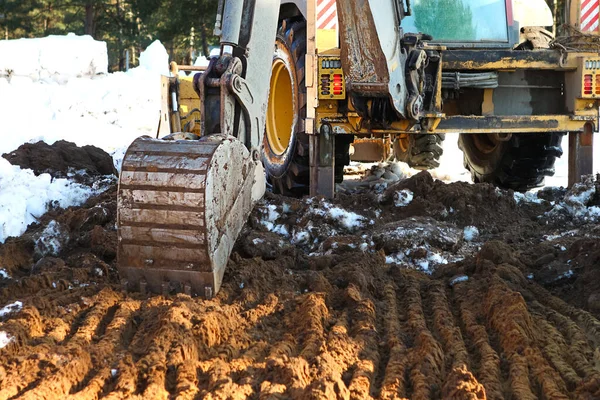Buldozer kovası inşaat için bir çukur kazıyor. Evin temeli, toprak işleri. Kazıcı bir kova ile toprağı kazar. Tarım, tarım.