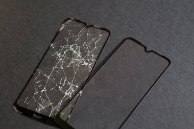 Akıllı telefonun için kırık cam. Telefon ekranı için koruyucu camda çatlaklar var. Siyah arka planda hasarlı ve yeni bir film. Boşluğu kopyala