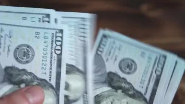 Kadınların elleri parayı sayar: Tahta bir masaya dolar koyar, banknotları çevirirler. Yüz dolar. Yakın plan 100 dolarlık banknotlar. Finans, ekonomi, mali planlama, ekonomi, tasarruflar.