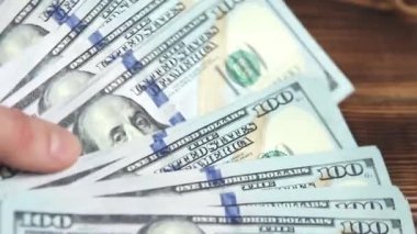 Kadınların elleri parayı sayar: Tahta bir masaya dolar koyar, banknotları çevirirler. Yüz dolar. Yakın plan 100 dolarlık banknotlar. Finans, ekonomi, mali planlama, ekonomi, tasarruflar.