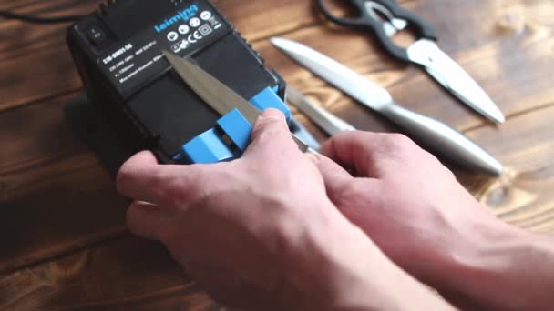 在家里的电动磨刀机上磨刀 男人的手把刀片夹在蓝色的磨刀机之间 灰尘在机器上飞扬 2021年4月25日 俄罗斯卡卢加 — 图库视频影像