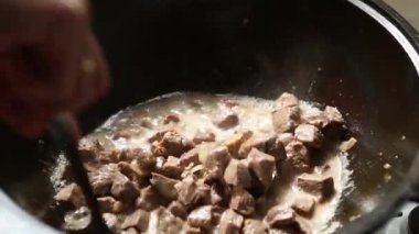 Aşçının eli slotlu kaşıkla sostaki et parçalarını sıcak buharla karıştırır. Dökme demir bir kazanda pilav pişirmek, zirvak, doğu mutfağı. Adım 1