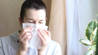 Evde bir kadın burnunu peçeteye siliyor. Soğuk algınlığı, kötü sağlık, baş ağrısı, burun tıkanıklığı, hapşırma belirtileri. Soğuk mevsim, ev tedavisi