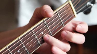 Bir adamın eli gitarın fretboard 'unda parmaklarını tellerde gezdirir ve akorları kıskaçlar. Enstrümantal müzik, notalar üzerine gitar dersi