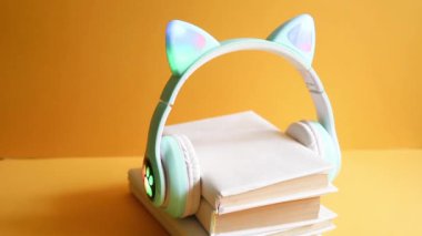 Çocuklar için sesli peri masalları, kedi kulaklı çocuk kulaklıklarının olduğu sesli kitap konsepti, sarı arka planda beyaz kapağa sarılı kağıt kitapları dinlemek. Eğitim ve eğlence.