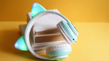 Çocuklar için sesli peri masalları, kedi kulaklı çocuk kulaklıklarının olduğu sesli kitap konsepti, sarı arka planda beyaz kapağa sarılı kağıt kitapları dinlemek. Eğitim ve eğlence.
