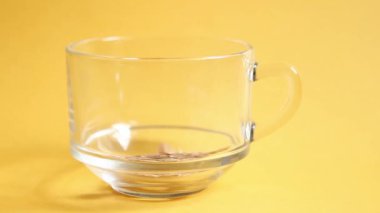 Sarı arka planda mısır ve çok tahıllı şeffaf kase. Taneler fincanın içine düşer. Hızlı ve sağlıklı kahvaltı.