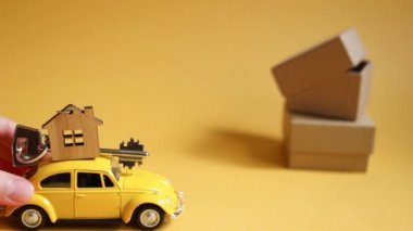 Çatıdaki evin anahtarı olan sarı oyuncak araba aydınlatıcı bir arka plana konuyor ve kutuları paketliyor. Yeni bir eve taşınmak, ipotek, daire almak, taksi tutmak. Uzayı kopyala Kaluga, Rusya, 08.04.21