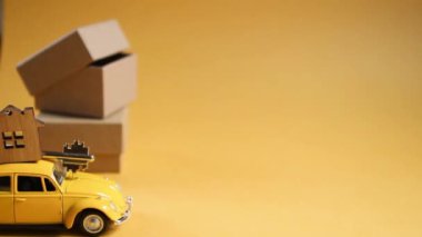 Çatıdaki evin anahtarı olan sarı oyuncak araba aydınlatıcı bir arka plana konuyor ve kutuları paketliyor. Yeni bir eve taşınmak, ipotek, daire almak, taksi tutmak. Uzayı kopyala Kaluga, Rusya, 08.04.21