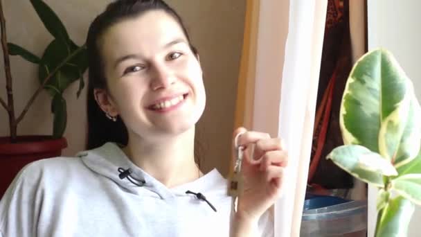 一个拿着房子钥匙坐在窗前的快乐女人 新家的梦想 买房子的快乐 抵押贷款 — 图库视频影像
