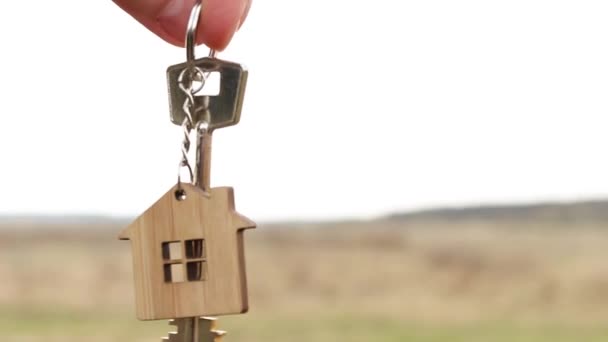 房子的木制挂件 手里拿着钥匙 天空和田野的背景 梦想着自己的家 在农村建起一座小木屋 进行规划和设计 交付项目 搬到新房子 — 图库视频影像