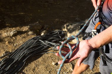 Bir erkek tırmanıcı piste tırmanmadan önce emniyet kemerine sekiz düğüm atar. Tırmanma ekipmanları: halat, hızlı silah çekme, güvenlik aygıtı, emniyet kemeri. Spor dağı turizmi, aktif yaşam tarzı, ekstrem sporlar