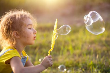 Kot tulumlu bir kız yazın gün batımında bir tarlada sabun köpüğü üflüyor. Uluslararası Çocuk Günü, mutlu çocuk, açık hava aktiviteleri. Yaz dönemi. Sağlıklı ve çevre dostu bir yaşam tarzı.