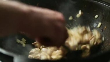 Aşçının elinde slotlu bir kaşıkla, soğanlı et parçaları karıştırılıyor. Yağ, dökme demir tavada kızartılıyor. Buhar geliyor, yağ kaynıyor. Et güveci, kazanda barbekü, yakın plan.