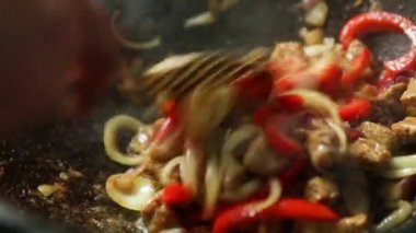 Aşçının eli kaşıkla kesilmiş sebzeleri karıştırıyor ve et yağda kızartılıyor ve baharatlar tavada kızartılıyor, buhar geliyor, yağ kaynıyor. Kazanda pişirme güveci, yakın plan.